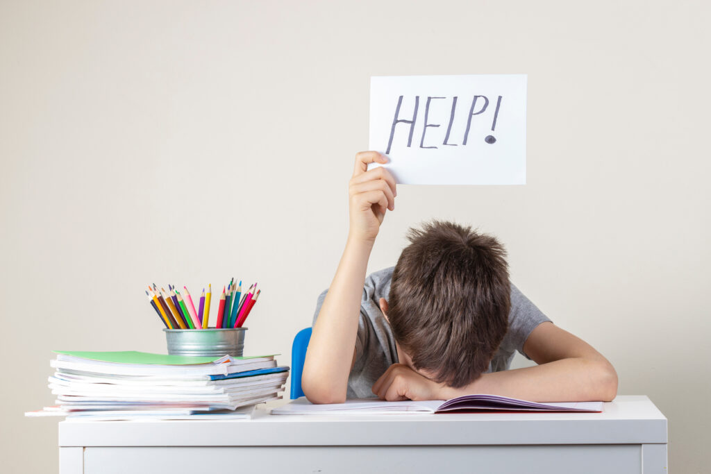 Child at a desk holding a sign that reads HELP!